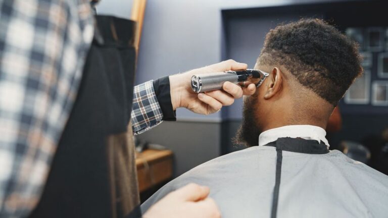 Andis Master Cordless vs Wahl Magic Clip: Fade Pick 7 Barber in a plaid shirt trimming the side of a bearded client's hair with a cordless trimmer