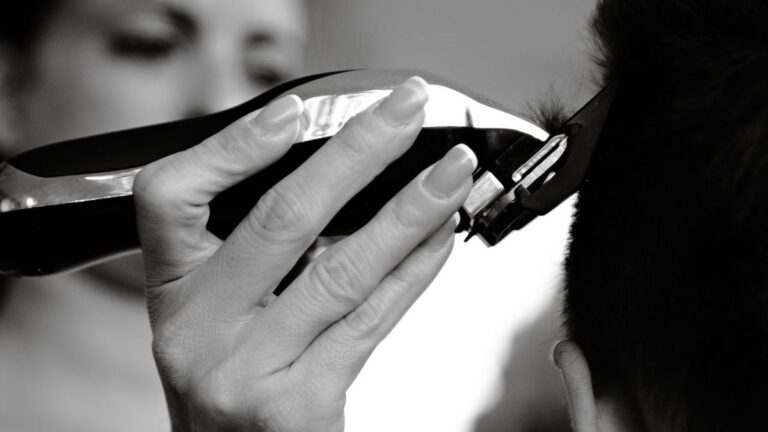Black and white close-up of a woman's hand guiding a clipper along a client's hairline
