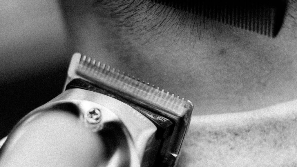 Black and white close-up of a clipper trimming the nape of a client's neck