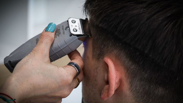 Best Clippers for Thick or Fine Hair (What Actually Matters) 9 Close-up of a hand using a grey clipper along the side of a man's head